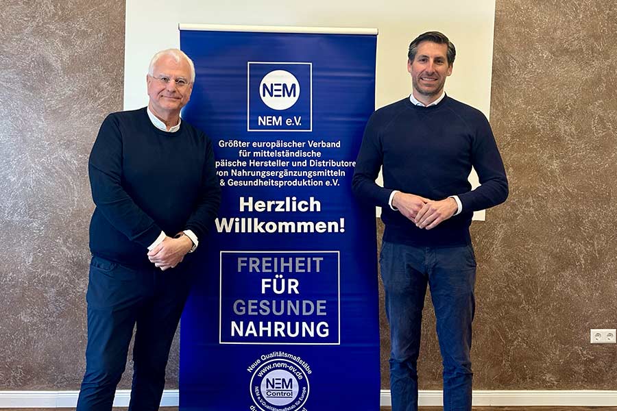 Dr. Christian Grosselfinger and Manfred Scheffler in front of a signage with the NEM Verband logo and more info.